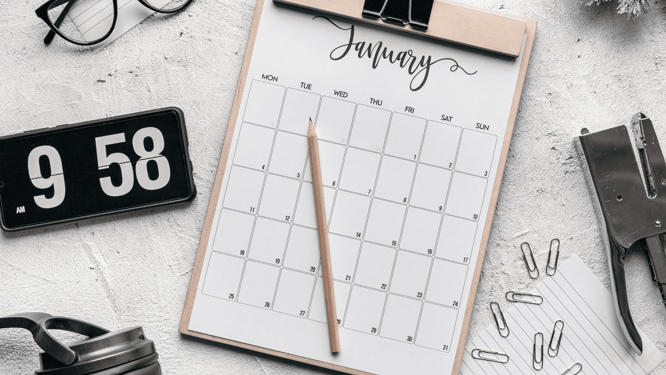 Graphical image of clipboard with January calendar, pencil on top of the calendar. Phone with clock to the left, various stationary items to the left on white background.