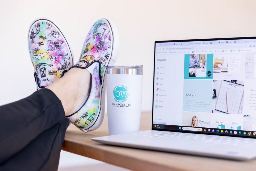 Colorful shoes on desk with mug and laptop.